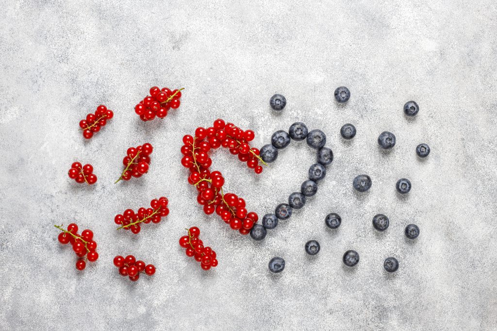 Napój antyoksydacyjny – czerwona porzeczka i borówki ułożone w kształt serca na szarym tle